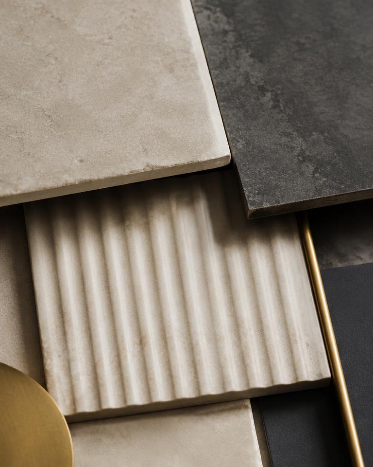 Cream fluted, warm stone and charcoal tile samples with brass accents