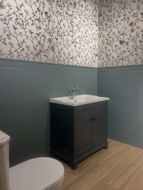 A dark vanity, soft blue panelling and floral wallpaper in a bathroom shared by Global Tiles & Bathrooms