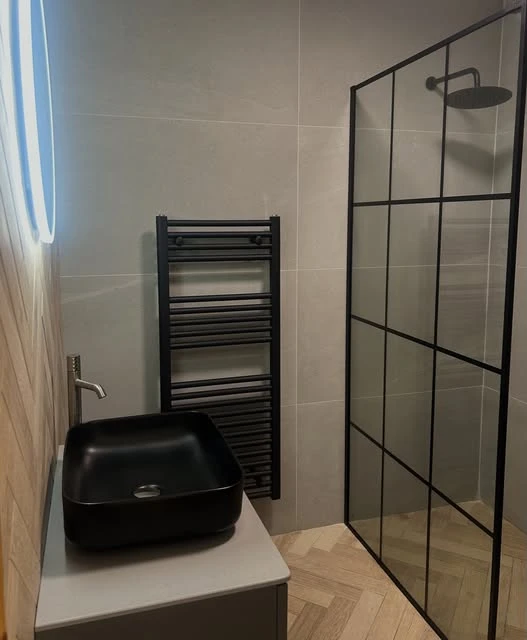 Stone-effect bathroom walls, a black basin and a framed shower screen shared by Global Tiles & Bathrooms
